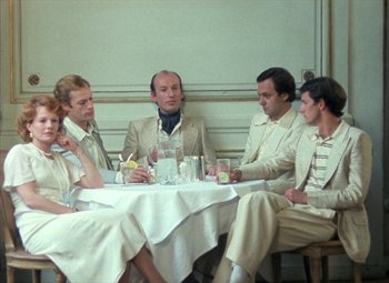 Movie still from “India Song” (1975), directed by Marguerite Duras – A group of people sitting around a table with drinks; Medium shot, High angle