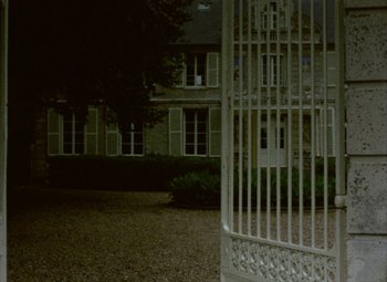 Movie still from “India Song” (1975), directed by Marguerite Duras – A white gate in front of a large building at night; Extreme Wide shot, Low angle