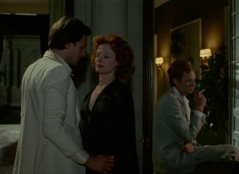 Movie still from “India Song” (1975), directed by Marguerite Duras – A man and a woman standing next to each other in front of another man; Medium shot, Over the shoulder angle