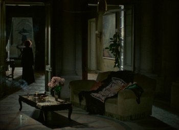 Movie still from “India Song” (1975), directed by Marguerite Duras – A living room filled with furniture next to a window; Wide shot, High angle