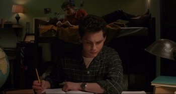 Movie still from “Indignation” (2016), directed by James Schamus – A man sitting at a table writing on a piece of paper; Medium shot, High angle