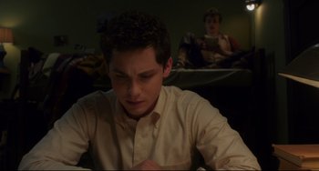 Movie still from “Indignation” (2016), directed by James Schamus – A young man sitting at a table writing on a piece of paper; Medium shot, High angle