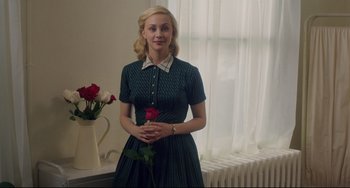 Movie still from “Indignation” (2016), directed by James Schamus – A young woman holding a red rose while standing next to a window; Medium shot, Over the shoulder angle