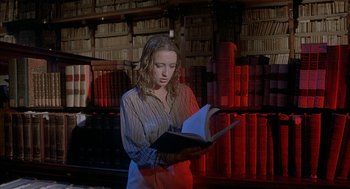 Movie still from “Inferno” (1980), directed by Dario Argento – A woman standing in front of stacks of books holding an open book; Medium shot, High angle