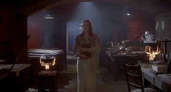 Movie still from “Inferno” (1980), directed by Dario Argento – A woman standing in a dimly - lit room holding a book; Wide shot, High angle