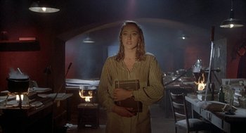 Movie still from “Inferno” (1980), directed by Dario Argento – A woman standing in a dimly - lit room holding a book; Medium shot, Low angle