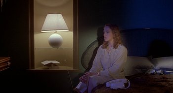 Movie still from “Inferno” (1980), directed by Dario Argento – A woman sitting on a chair in front of a lamp; Medium shot, High angle