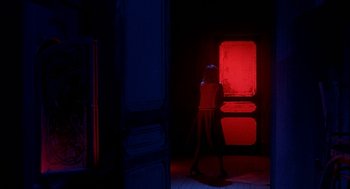Movie still from “Inferno” (1980), directed by Dario Argento – A person standing in a room with a red light; Wide shot, Over the shoulder angle