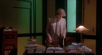 Movie still from “Inferno” (1980), directed by Dario Argento – An older man in a white suit is standing at a table with a bunch of books; Medium shot, Low angle