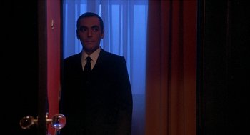 Movie still from “Inferno” (1980), directed by Dario Argento – A man wearing a suit and tie standing in front of a window; Medium shot, Low angle