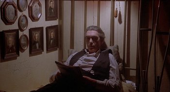 Movie still from “Inferno” (1980), directed by Dario Argento – A man sitting in a chair reading a book; Medium shot, High angle