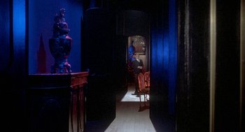 Movie still from “Inferno” (1980), directed by Dario Argento – A man sitting on a chair next to a table; Wide shot, Over the shoulder angle