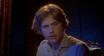 Movie still from “Inferno” (1980), directed by Dario Argento – A man with long blonde hair is sitting in the dark; Close Up shot, High angle