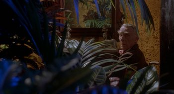 Movie still from “Inferno” (1980), directed by Dario Argento – An older man sitting in a room with plants; Medium shot, Over the shoulder angle