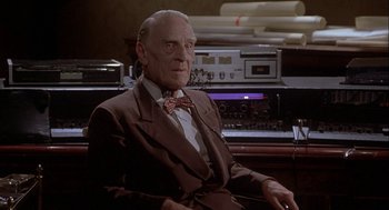 Movie still from “Inferno” (1980), directed by Dario Argento – An older man sitting in a chair in front of a desk; Close Up shot, Low angle
