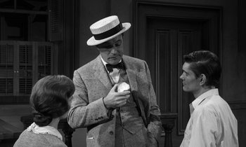 Movie still from “Inherit the Wind” (1960), directed by Stanley Kramer – A man in a suit and a hat is looking at a cupcake; Medium shot, Over the shoulder angle