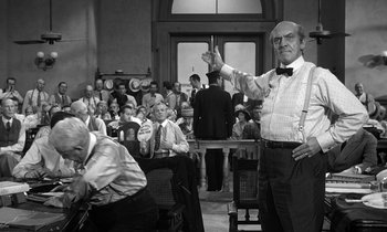 Movie still from “Inherit the Wind” (1960), directed by Stanley Kramer – An old photo of a man in a bow tie holding up one finger; Medium shot, Over the shoulder angle