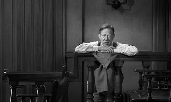 Movie still from “Inherit the Wind” (1960), directed by Stanley Kramer – An older man sitting at a table with his arms crossed; Medium shot, High angle