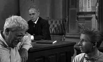 Movie still from “Inherit the Wind” (1960), directed by Stanley Kramer – An older man sitting at a desk with two other people; Medium shot, Over the shoulder angle