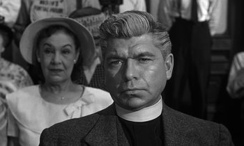 Movie still from “Inherit the Wind” (1960), directed by Stanley Kramer – A man in a priest's outfit with a woman in a crowd behind him; Close Up shot, Low angle