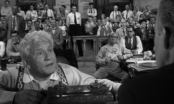 Movie still from “Inherit the Wind” (1960), directed by Stanley Kramer – An old man sitting in a courtroom with a bunch of people in the background; Medium shot, Over the shoulder angle