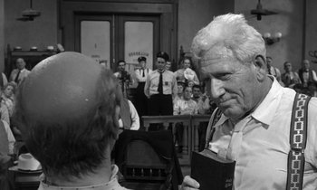 Movie still from “Inherit the Wind” (1960), directed by Stanley Kramer – An older man holding a book in front of a group of people; Close Up shot, Over the shoulder angle