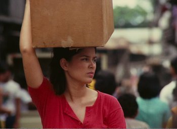 A woman in a red shirt carrying a brown bag on top of her head