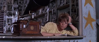 Movie still from “Inside Daisy Clover” (1965), directed by Robert Mulligan – A woman sitting at a table reading a book; Medium shot, High angle