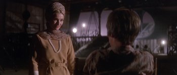 Movie still from “Inside Daisy Clover” (1965), directed by Robert Mulligan – A woman wearing a dress and a head scarf is talking to a man in front of a bridge; Medium shot, Low angle