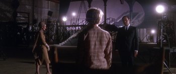 Movie still from “Inside Daisy Clover” (1965), directed by Robert Mulligan – A man standing in front of stairs at night; Wide shot, Over the shoulder angle