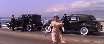 Movie still from “Inside Daisy Clover” (1965), directed by Robert Mulligan – An older woman walking down the street in front of old cars; Wide shot, Low angle