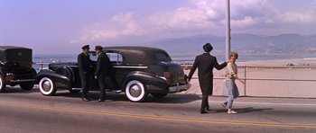 Movie still from “Inside Daisy Clover” (1965), directed by Robert Mulligan – A couple of men standing next to an old black car; Wide shot, High angle