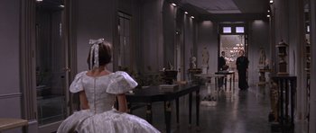 Movie still from “Inside Daisy Clover” (1965), directed by Robert Mulligan – A woman in a white dress sitting in front of a table; Wide shot, Over the shoulder angle