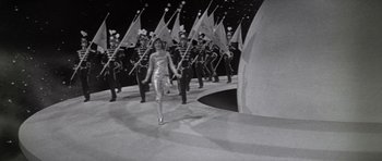 Movie still from “Inside Daisy Clover” (1965), directed by Robert Mulligan – A group of people marching on a stage with flags; Wide shot, High angle