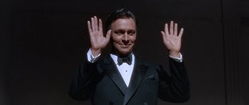 Movie still from “Inside Daisy Clover” (1965), directed by Robert Mulligan – A man wearing a tuxedo and a bow tie holding his hands up in the air; Medium shot, Low angle