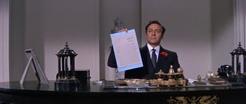 Movie still from “Inside Daisy Clover” (1965), directed by Robert Mulligan – A man in a suit holding up a piece of paper in front of him; Medium shot, Low angle
