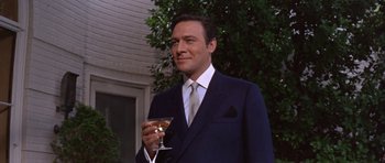 Movie still from “Inside Daisy Clover” (1965), directed by Robert Mulligan – A man in a suit and tie holding a glass of wine; Medium shot, Low angle