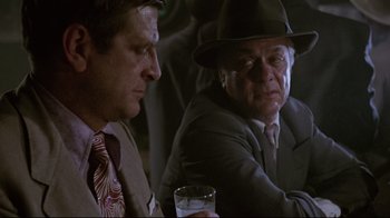 Movie still from “Insignificance” (1985), directed by Nicolas Roeg – Two men sitting next to each other holding a glass; Close Up shot, Over the shoulder angle