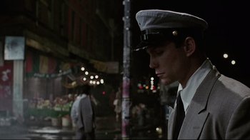 Movie still from “Insignificance” (1985), directed by Nicolas Roeg – A man wearing a hat standing on a city street at night; Close Up shot, Low angle