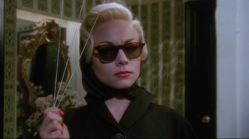 Movie still from “Insignificance” (1985), directed by Nicolas Roeg – A woman in a black coat and sunglasses holding a string; Close Up shot, Low angle
