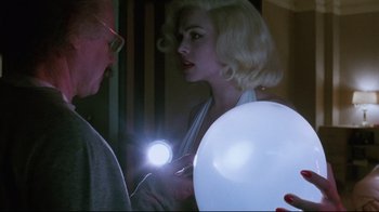 Movie still from “Insignificance” (1985), directed by Nicolas Roeg – A woman holding a white balloon while a man looks on; Medium shot, Over the shoulder angle