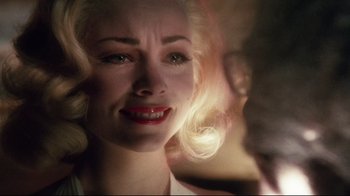 Movie still from “Insignificance” (1985), directed by Nicolas Roeg – A woman with blonde hair and red lipstick looking sad; Close Up shot, Over the shoulder angle