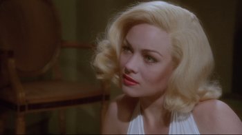 Movie still from “Insignificance” (1985), directed by Nicolas Roeg – A woman with blonde hair sitting in front of a chair; Close Up shot, Over the shoulder angle