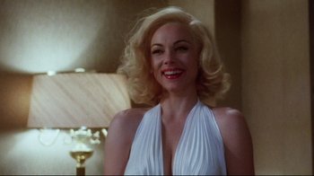 Movie still from “Insignificance” (1985), directed by Nicolas Roeg – A woman in a white dress smiling for the camera; Close Up shot, Over the shoulder angle