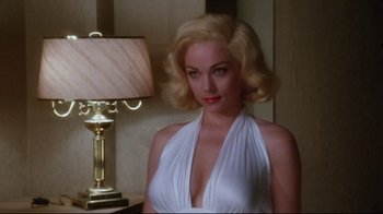 Movie still from “Insignificance” (1985), directed by Nicolas Roeg – A woman in a white dress standing in front of a lamp; Medium shot, Over the shoulder angle