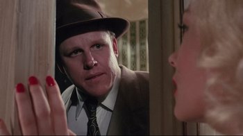 Movie still from “Insignificance” (1985), directed by Nicolas Roeg – A man wearing a suit and hat looking at a woman in the mirror; Close Up shot, Over the shoulder angle