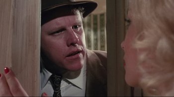 Movie still from “Insignificance” (1985), directed by Nicolas Roeg – A man wearing a suit and tie talking to a woman wearing a hat; Close Up shot, Over the shoulder angle