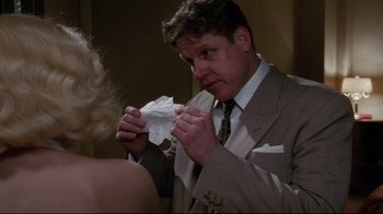 Movie still from “Insignificance” (1985), directed by Nicolas Roeg – A man in a suit and tie holding a piece of paper in his hand; Medium shot, Over the shoulder angle