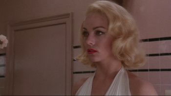 Movie still from “Insignificance” (1985), directed by Nicolas Roeg – A woman with blonde curly hair and red lipstick; Close Up shot, Over the shoulder angle