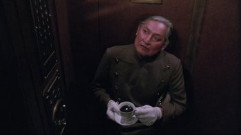 Movie still from “Insignificance” (1985), directed by Nicolas Roeg – A man in a uniform holding a cup of coffee; Medium shot, Low angle